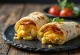 Bánh cuộn ăn sáng với trứng, thịt xông khói, xà lách và phô mai, cuộn trong vỏ tortilla, cắt đôi theo đường chéo